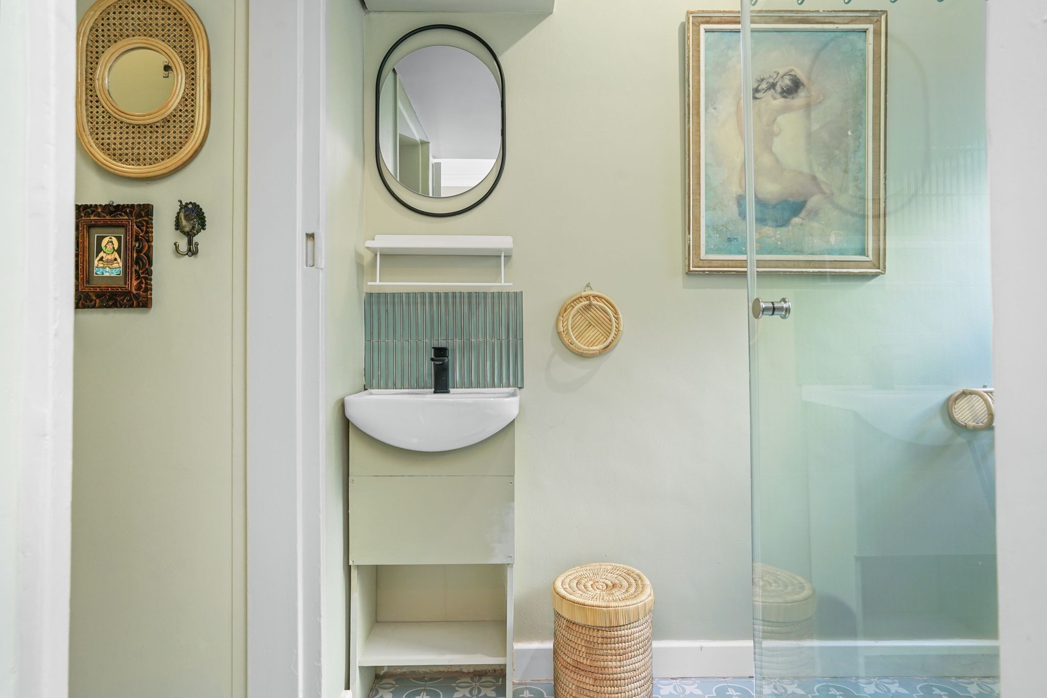 A bathroom with a white sink, a mirror, a framed picture, and a glass shower door.