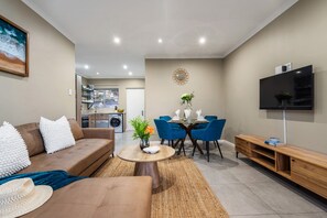 A modern living room with a brown sofa, a coffee table, and a dining area with blue chairs.