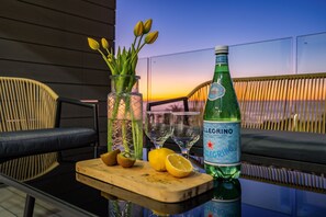 A table with a bottle of liquor, glasses, a cutting board with fruit, and a vase with flowers. - Brighton Court (Cape Town)