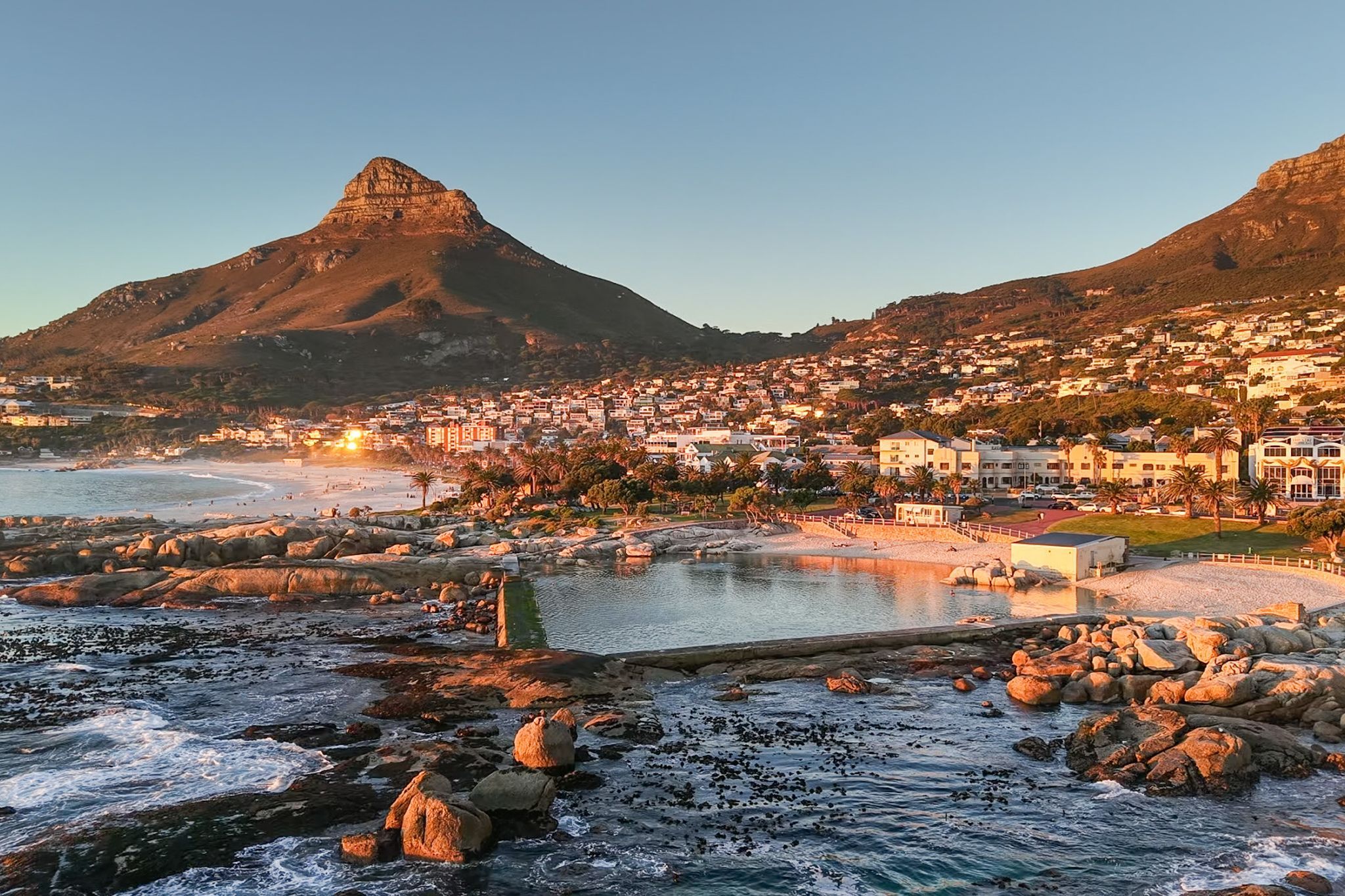A coastal town with a prominent mountain, a beach, and a calm sea.