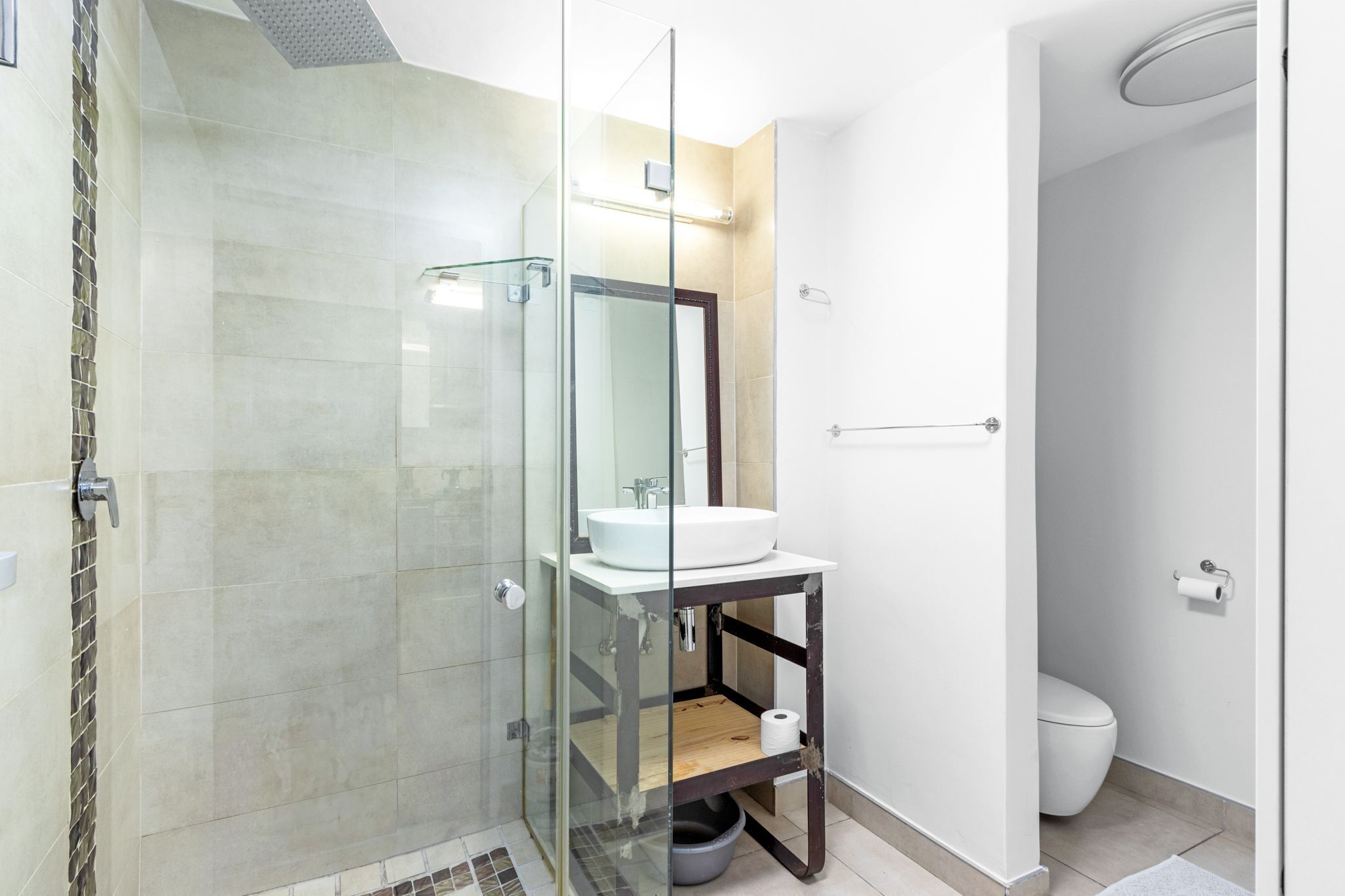 Une salle de bain moderne avec une douche à parois de verre, un lavabo blanc posé sur une étagère en bois et des toilettes.