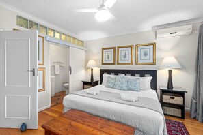 A neatly arranged bedroom with a bed, bedside tables, a nightstand, a bench, and a ceiling fan. - Firdale Mews 5 (Cape Town)