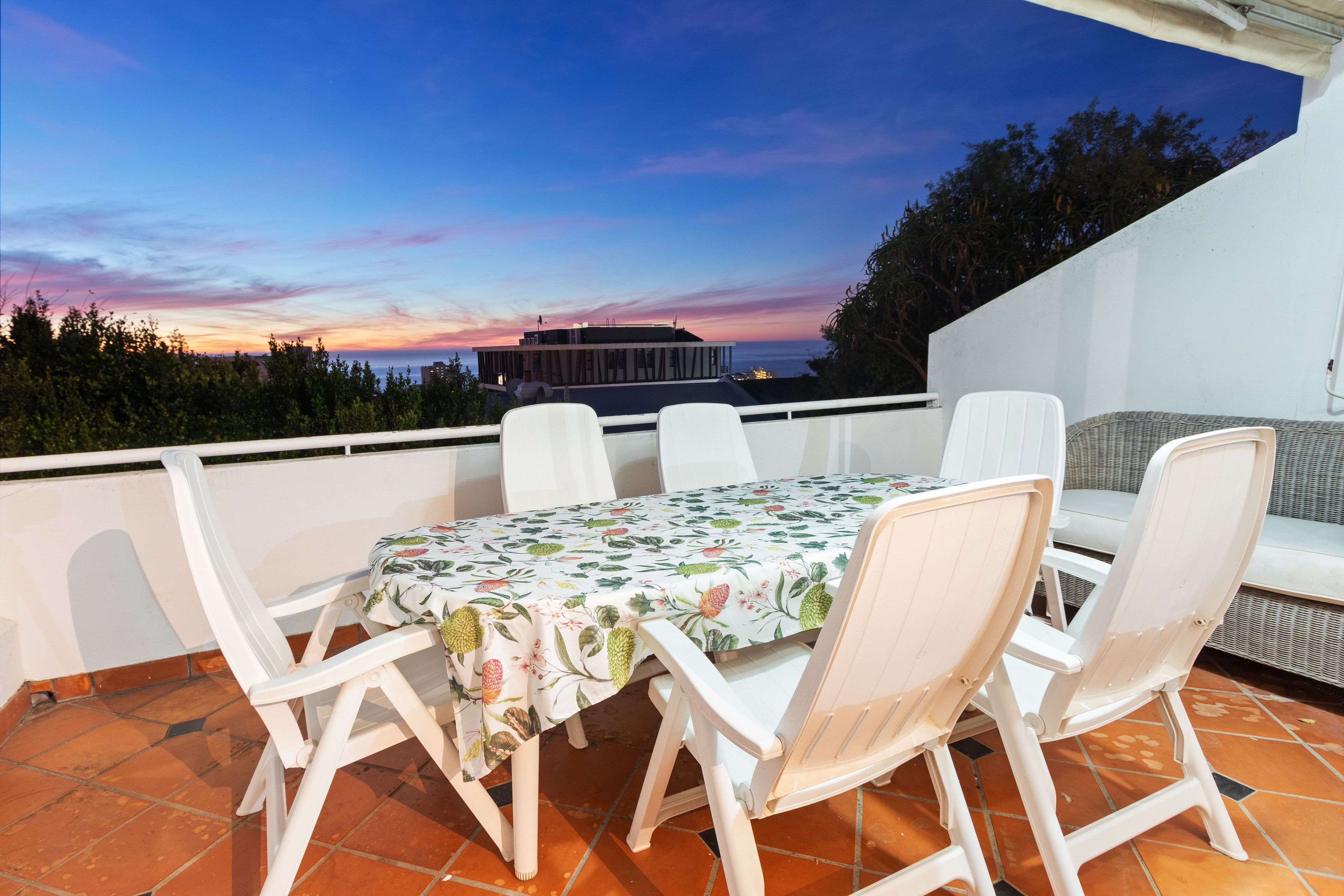 Une terrasse avec une table et des chaises, une vue sur le coucher de soleil et un bâtiment en arrière-plan.