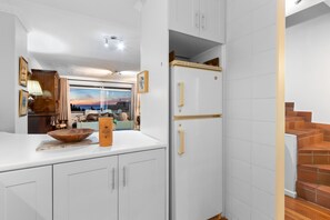 A kitchen with white cabinets, a wooden bowl on the counter, and a white refrigerator with gold handles. - Firdale Mews 5 (Cape Town)