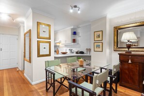 A dining area with a glass table and chairs, a wooden cabinet, and framed pictures on the walls. - Firdale Mews 5 (Cape Town)