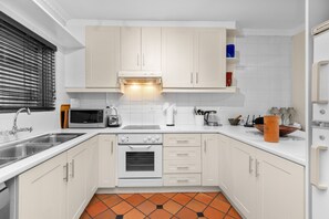 A modern kitchen with white cabinets, a built-in oven, a microwave, and a sink. - Firdale Mews 5 (Cape Town)