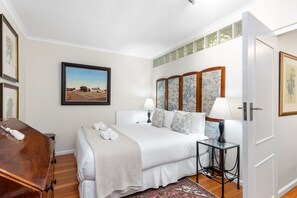 A neatly arranged bedroom with a bed, bedside tables, a wooden dresser, and a framed painting on the wall. - Firdale Mews 5 (Cape Town)