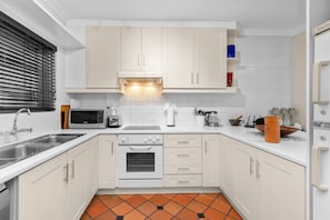 A modern kitchen with white cabinets, a built-in oven, a microwave, and a sink. - Firdale Mews 5 (Cape Town)