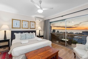 A modern bedroom with a large bed, a ceiling fan, and a city view through floor-to-ceiling windows. - Firdale Mews 5 (Cape Town)