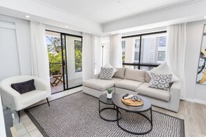A modern living room with a sectional sofa, a round coffee table, and a view of the outdoors through large windows. - Sausalito 201 (Cape Town)