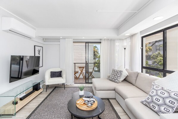 A modern living room with a sofa, a coffee table with snacks, a TV, and a balcony with a view. - Sausalito 201 (Cape Town)