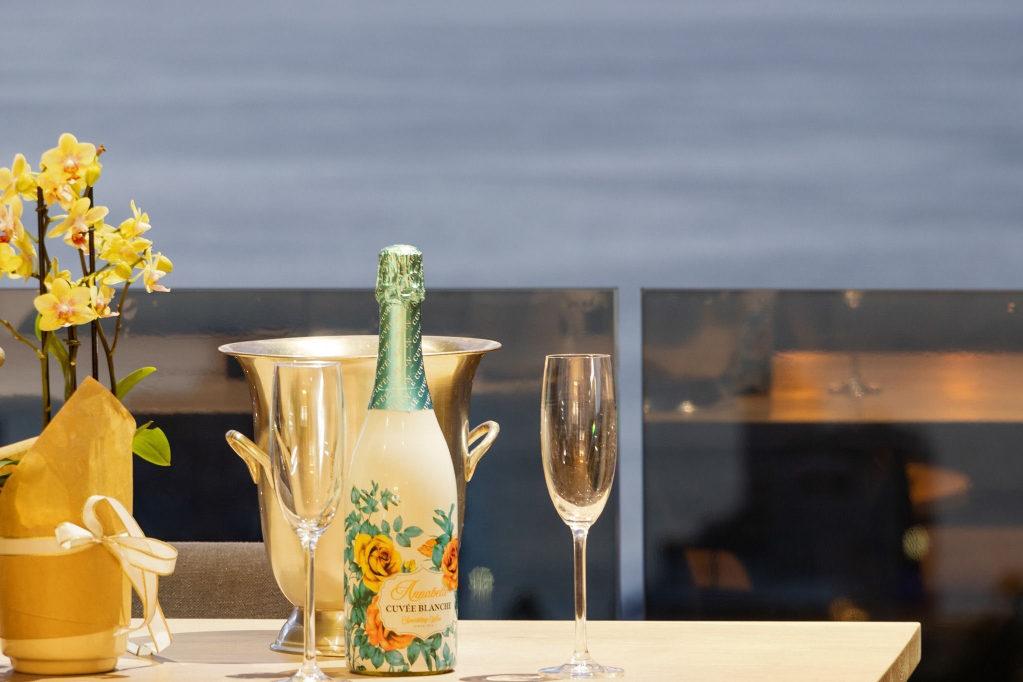 A table with a champagne bottle, a glass, and a vase with flowers.
