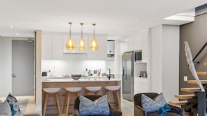 A modern kitchen with a central island, bar stools, pendant lighting, and a staircase with a wooden finish. - Elements on Battery (Cape Town)
