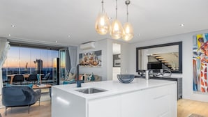 A modern kitchen with a large island, pendant lighting, and a view of the cityscape. - Elements on Battery (Cape Town)