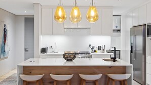 A modern kitchen with a central island, white cabinetry, stainless steel appliances, and three pendant lights. - Elements on Battery (Cape Town)