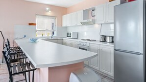 A modern kitchen with white cabinets, a stainless steel refrigerator, and a central island with seating. - Summerville 20 (Cape Town)