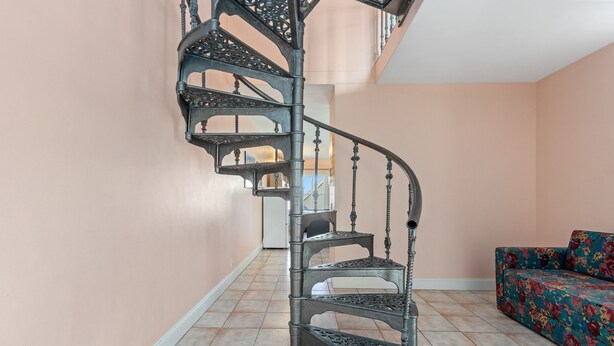 Una escalera en espiral con barandillas metálicas decoradas en una habitación con paredes color melocotón y un sofá floral.