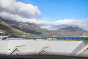 Een kusthotel met een metalen dak, met uitzicht op een bergachtig landschap en de oceaan.