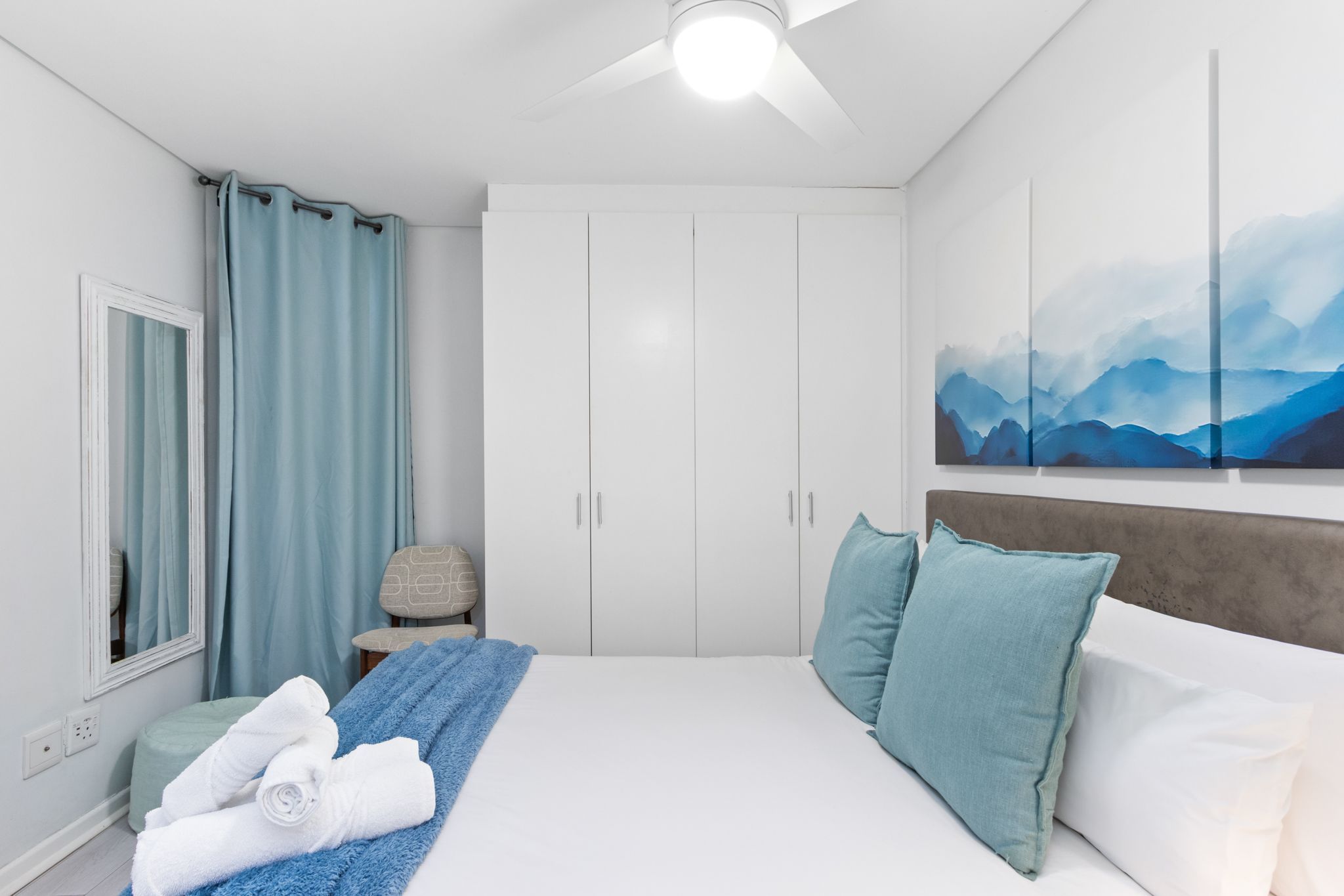 A bedroom with a bed, a wardrobe, a painting, and a ceiling fan.
