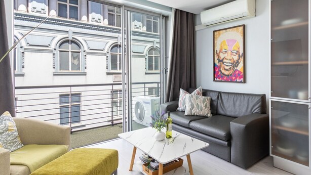 A modern living room with a sofa, a coffee table, and a view of a building with large windows. - Green Market Place (Cape Town)