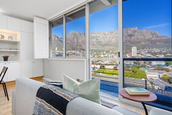 A modern living room with a large window, white cabinetry, and a view of a city and mountains. - Perspectives 1107 (Cape Town)
