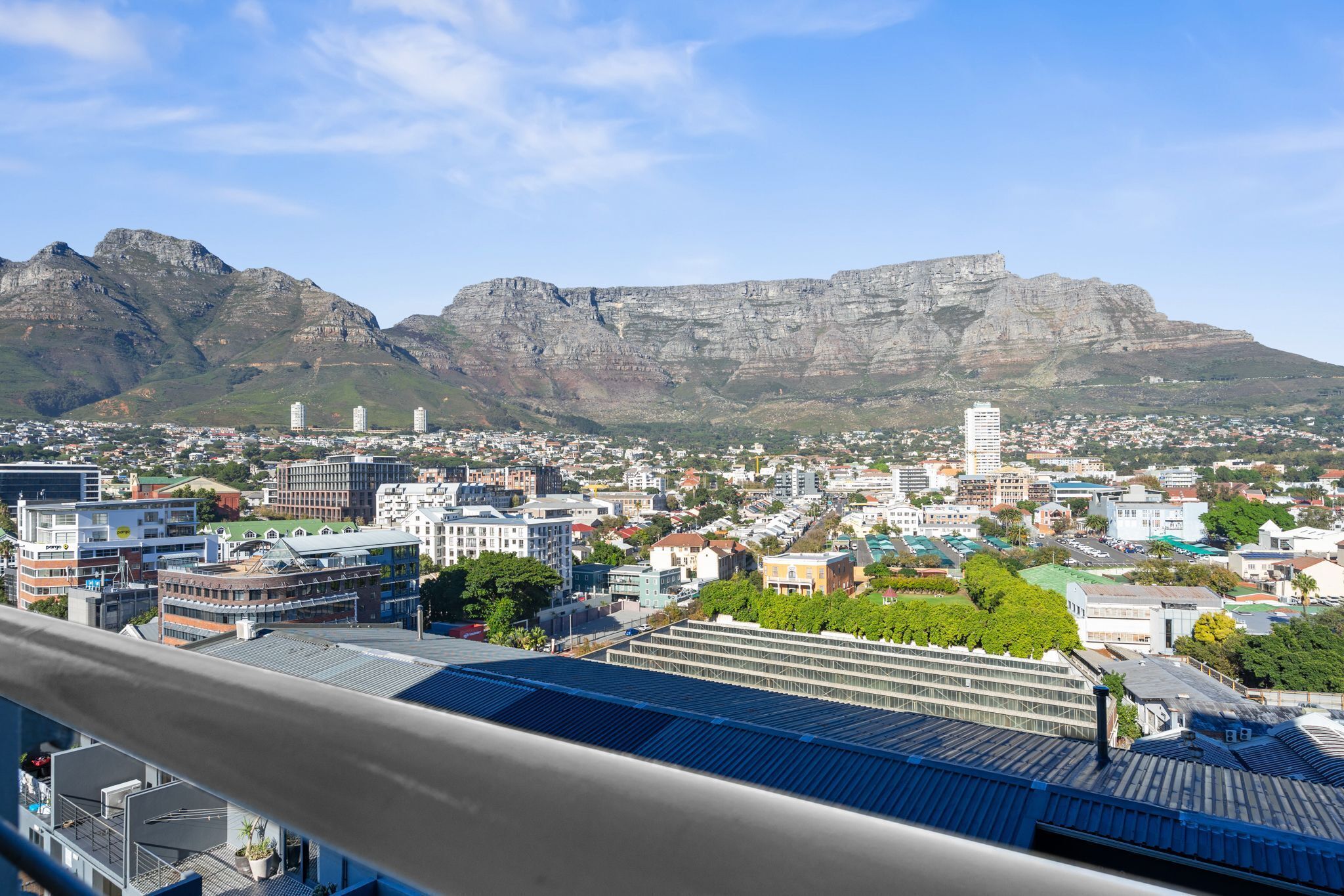 Un paisaje urbano con una imponente cordillera al fondo, edificios modernos y cielo despejado.