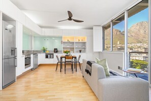 A modern kitchen with white cabinets, a dining area with a table and chairs, and a large window with a city view. - Perspectives 1107 (Cape Town)