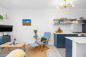 A modern kitchen with a built-in stove, white cabinets, and a wooden dining table. - Summerville Beach Loft (Cape Town)