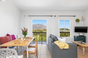 A modern living room with a balcony, a dining area with a table set for two, and a television on a stand. - Summerville Beach Loft (Cape Town)