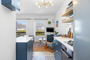 A modern kitchen with a dining area, a TV, and a view of mountains. - Summerville Beach Loft (Cape Town)