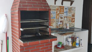 Un horno exterior de ladrillo con un estante encima, un escoba y una mopa apoyados contra la pared.