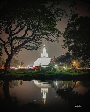 A white dome structure with a spire, surrounded by trees and a calm body of water reflecting the structure. - Impress Holiday Home (Anuradhapura)