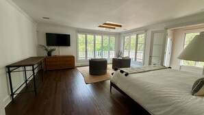 Un dormitorio con una cama grande, un escritorio de madera, un televisor y una ventana con vista a follaje.