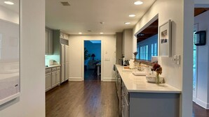 Una cocina moderna con armarios blancos, piso de madera y vista al comedor.