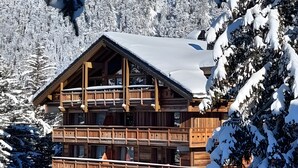 Eine mehrstöckige Holzhütte mit Balkonen, umgeben von schneebedeckten Bäumen und Bergen.