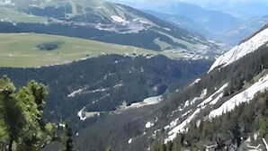 Eine gebirgige Landschaft mit einem Tal, Bäumen und schneebedeckten Hängen.