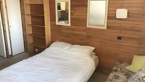 Ein Schlafzimmer mit Holzwand, einem Bett, einem Nachttisch, einem Spiegel und einem Kleiderschrank.