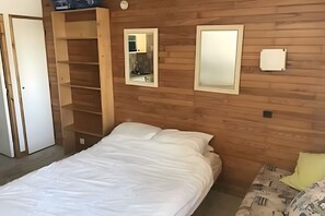 A bedroom with a wooden wall, a bed, a nightstand, a mirror, and a wardrobe.
