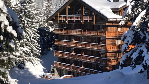 Eine mehrstöckige Holzhütte mit Balkonen, umgeben von schneebedeckten Bäumen.
