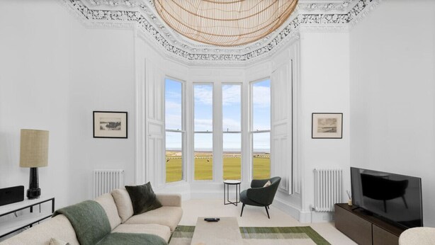 A spacious living room with a large bay window, a sofa, a television, and a dining area.