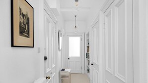 A narrow hallway with white walls, a radiator, a framed picture, a door at the end, and a small table with a book.