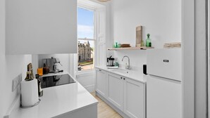 A modern kitchen with white cabinetry, a built-in oven, a sink, and a window offering a view of the street.