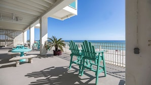A covered outdoor area with a view of the beach, featuring turquoise chairs and a table. - 308 Beachfront Condo with Pool Sunset Views (panama city beach)