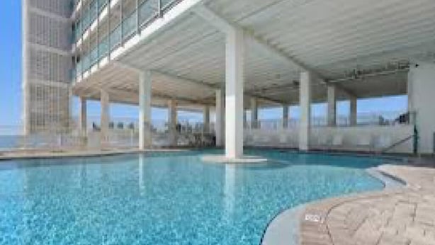 A swimming pool with a clear blue water surface, surrounded by a white structure with multiple levels and columns. - 308 Beachfront Condo with Pool Sunset Views (panama city beach)