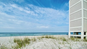 A beach with a white building featuring a lattice facade. - 308 Beachfront Condo with Pool Sunset Views (panama city beach)