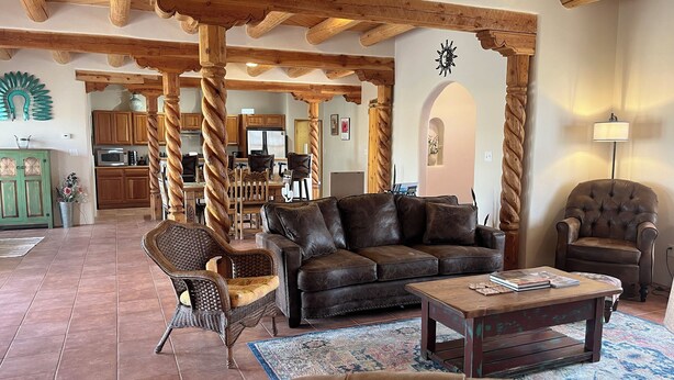 A spacious living area with a wooden ceiling, a brown leather sofa, a coffee table, and a dining area in the background. - Cosmic Cantina - Easy Stays and Great Location! (El Prado)