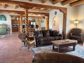 Un vaste espace de vie doté d’un plafond en bois, d’un canapé en cuir marron, d’une table basse et, au fond, d’un coin repas.