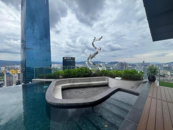A rooftop infinity pool with a curved edge, surrounded by greenery and a cityscape view.