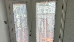 Una habitación con dos puertas blancas, cortinas de encaje, piso de madera y una pared blanca lisa.