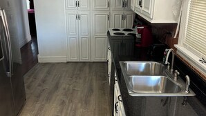 Una cocina con armarios blancos, encimera negra, electrodomésticos de acero inoxidable y suelo de madera.